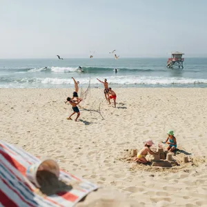 A beach scene: adults playing volleyball, kids building sandcastles, and surfers riding waves. - Ideogram Ideogram 4.0 (Quality)