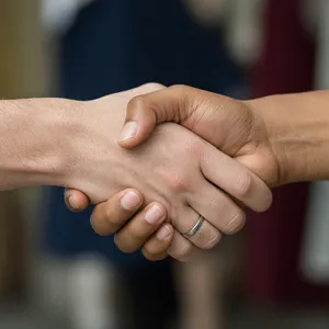 A close-up of two people shaking hands, both hands fully visible with five fingers each, in sharp focus against a blurred background. - XAI Grok Imagine (Quality)