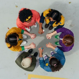 A group of five people joining hands in a circle, seen from above. - XAI Grok Imagine (Quality)