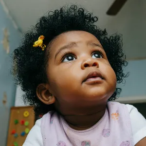 A hyper-realistic photo of a toddler with curly hair and big eyes, looking upward. - XAI Grok Imagine (Quality)