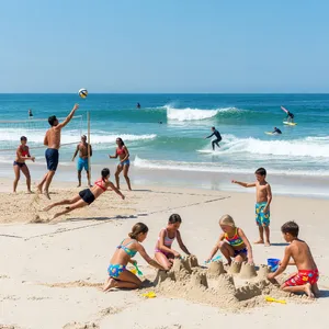 A beach scene: adults playing volleyball, kids building sandcastles, and surfers riding waves. - XAI Grok Imagine