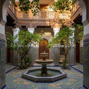 A traditional Moroccan riad courtyard with detailed zellige tilework, flowing fountain, citrus trees, and ornate woodwork. Morning light casting intricate shadow patterns. - XAI Grok Imagine