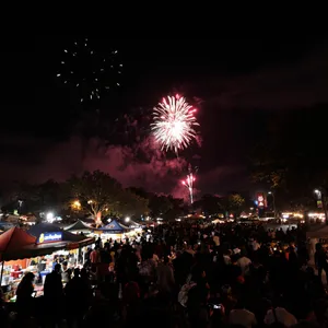 A nighttime festival with fireworks in the sky, food stalls lined up, and crowds mingling. - Black Forest Labs Flux 1.1 Pro Ultra