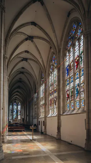 A Gothic cathedral interior at sunset with light streaming through detailed stained glass windows, creating colored patterns on stone floors and columns. Show accurate ribbed vaulting. - Ideogram Ideogram 4.0 (Quality)