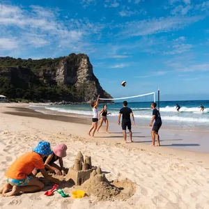 A beach scene: adults playing volleyball, kids building sandcastles, and surfers riding waves. - Recraft Recraft V4.1