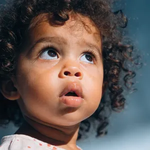 A hyper-realistic photo of a toddler with curly hair and big eyes, looking upward. - Recraft Recraft V4.1