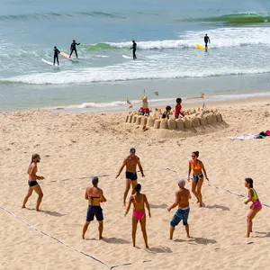 A beach scene: adults playing volleyball, kids building sandcastles, and surfers riding waves. - Reve Reve Image (Halfmoon)