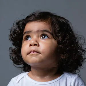 A hyper-realistic photo of a toddler with curly hair and big eyes, looking upward. - Reve Reve Image (Halfmoon)