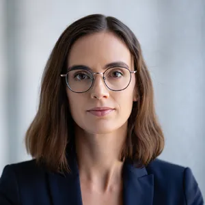 A professional headshot of a businesswoman wearing glasses, against a blurred background. - Reve Reve Image (Halfmoon)