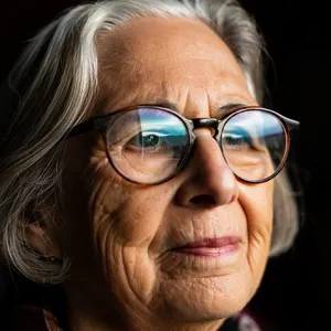 A ultra high-resolution portrait of an elderly woman with silver hair and bifocal glasses, each lens reflecting a distant landscape, captured in warm late-afternoon sunlight - Reve Reve Image (Halfmoon)