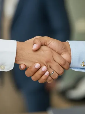 A close-up of two people shaking hands, both hands fully visible with five fingers each, in sharp focus against a blurred background. - XAI Grok Imagine (Quality)