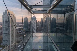 Photorealistic rendering of a contemporary glass skybridge between two skyscrapers, seen from inside with city views visible through glass walls and floor. Show accurate reflections and structural details. - XAI Grok Imagine (Quality)