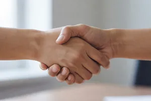A close-up of two people shaking hands, both hands fully visible with five fingers each, in sharp focus against a blurred background. - XAI Grok Imagine