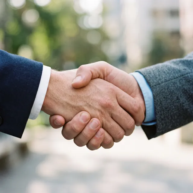 A close-up of two people shaking hands, both hands fully visible with five fingers each, in sharp focus against a blurred background. - Nano Banana 2.1