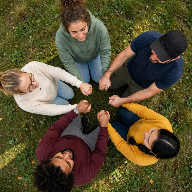 A group of five people joining hands in a circle, seen from above. - Muse Image
