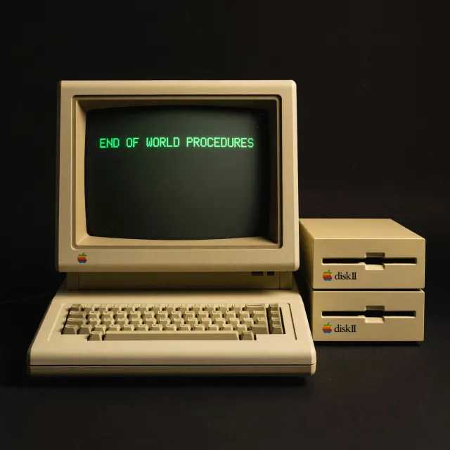 Vintage Apple II computer with green monochrome CRT screen, displaying 'END OF WORLD… - XAI Grok Imagine