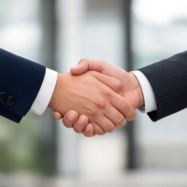 A close-up of two people shaking hands, both hands fully visible with five fingers each, in sharp focus against a blurred background. - Reve 2.1