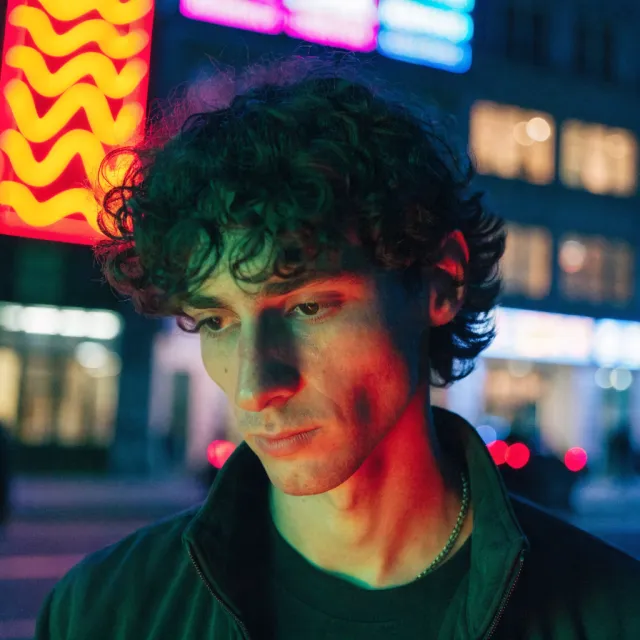 A nighttime portrait of a man lit by neon signs on a city street - Recraft V4.1