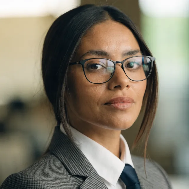 A professional headshot of a businesswoman wearing glasses, against a blurred background. - Recraft V4.1
