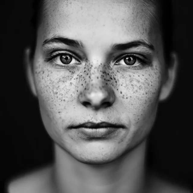 A black and white close-up portrait of a freckled woman with an intense gaze - Reve Image (Halfmoon)