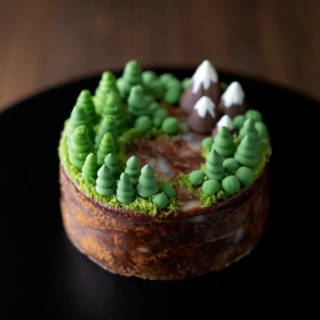 A dessert cake that looks like a tiny planet, complete with miniature trees and… - Reve Image (Halfmoon)
