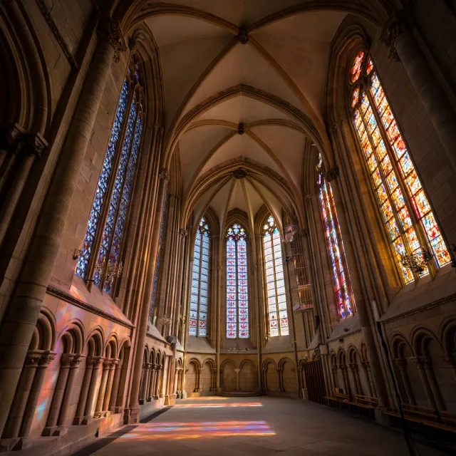 A Gothic cathedral interior at sunset with light streaming through detailed stained glass windows, creating colored patterns on stone floors and columns. Show accurate ribbed vaulting. - Reve Image (Halfmoon)