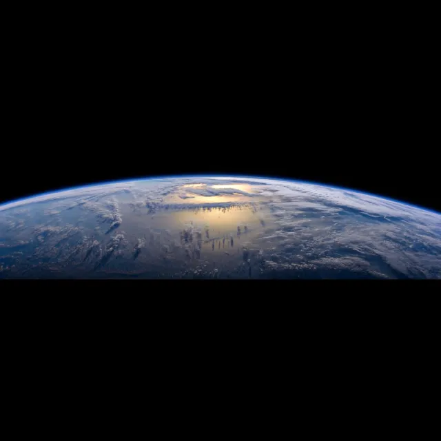 Photorealistic aerial photograph clearly showing the edge of the Earth from space, capturing realistic curvature, atmosphere, and sunlight reflections - Reve Image (Halfmoon)